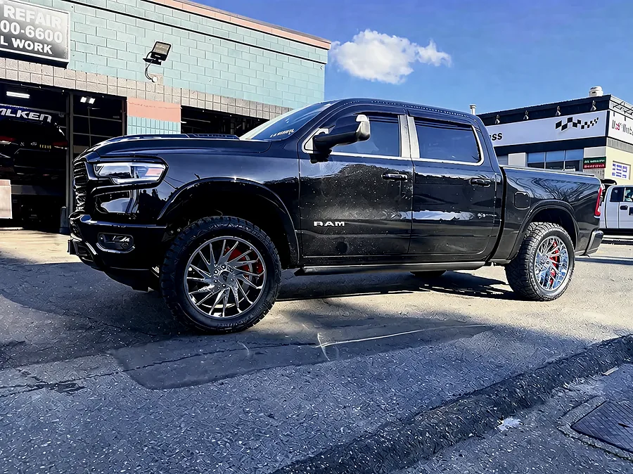Lifted black Ram pickup on polished multi-spoke wheels outside the shop